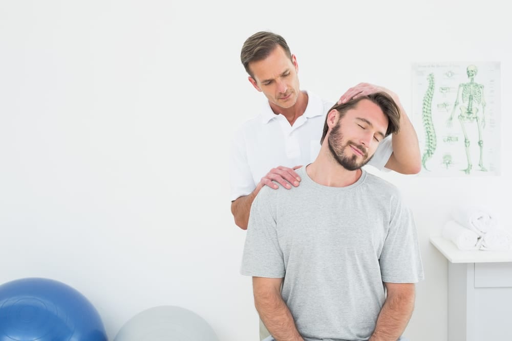 Quiropráctico titulado ajustando suavemente el cuello de un paciente masculino durante un tratamiento de manipulación espinal para el dolor de espalda o la recuperación de lesiones por accidente de tráfico.