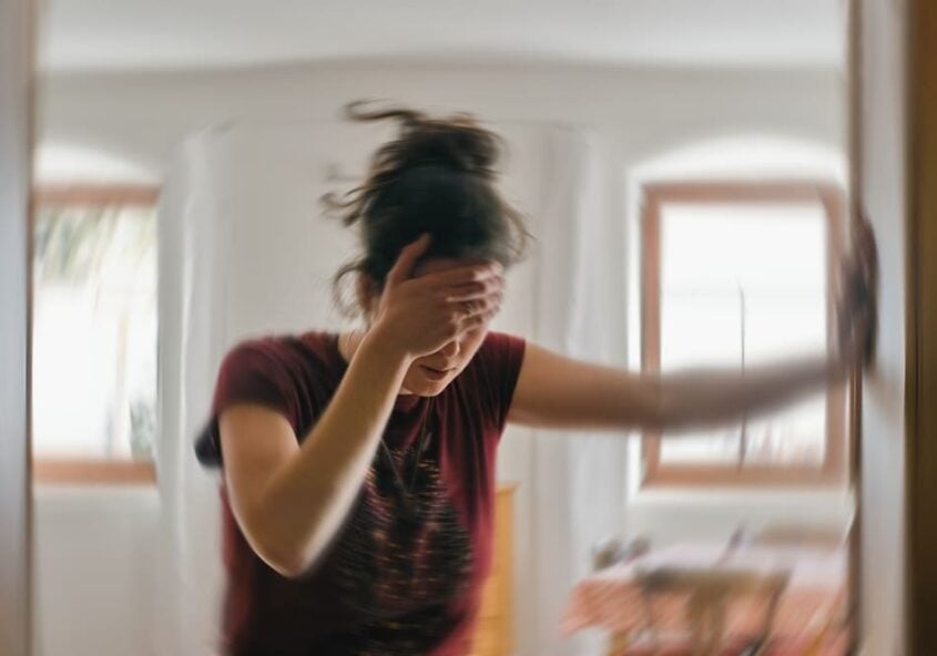 Mujer sosteniéndose la cabeza con angustia debido a la sensación de mareo y los síntomas de vértigo, lo que ilustra la necesidad de fisioterapia y rehabilitación vestibular.
