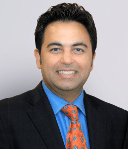 Dr. Manoj Sadhnani - Board-Certified Podiatric Physician & Surgeon Д-р Манодж Саднани, сертифицированный подиатр и хирург в Metro Health NYC, профессиональный портрет в белом халате; специализируется на лечении стоп и голеностопных суставов