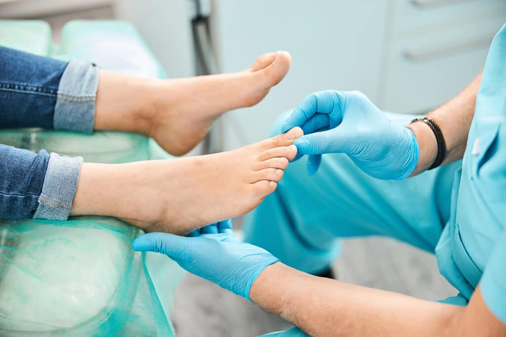 Un podólogo con guantes azules examina el pie y los dedos de un paciente durante una consulta en Metro Healthcare Partners, en Brooklyn (Nueva York).