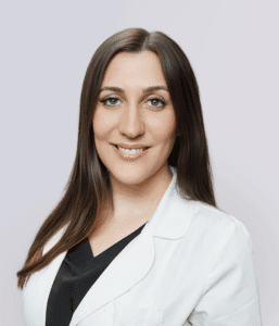 Chelsea Camarda Family Nurse Practitioner at Metro Healthcare Partners Профессиональный портрет Челси Камарда, семейной медсестры-практика, улыбающейся в белом халате в Metro Healthcare Partners, Бруклин, Нью-Йорк