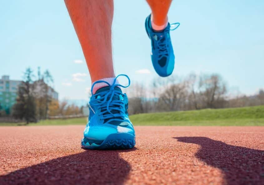 Primer plano de zapatillas deportivas y pies en movimiento en una pista, que ilustra los factores de riesgo comunes del pie de atleta (tinea pedis) en personas activas.