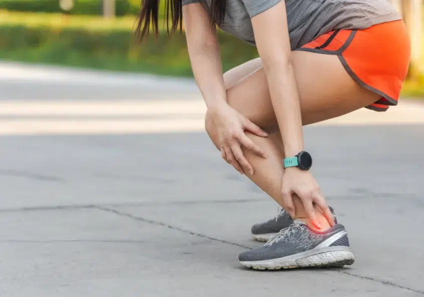 Una joven que experimenta un dolor agudo en el tendón de Aquiles mientras camina por una calle de la ciudad, lo que pone de relieve un síntoma común de la tendinitis de Aquiles.